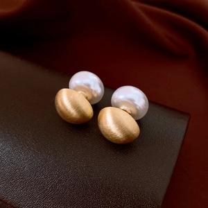 Close-up of golden brushed metal stud earring with white pearl on silk fabric