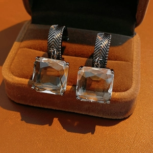 Détail de boucles d'oreilles carrées en verre argenté dans un écrin en velours