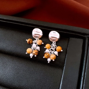 Close-up of 18K gold-plated earring with brown stone beads and white pearls on leather