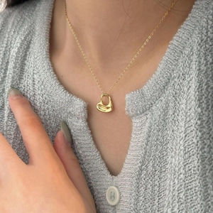Close-up of a 18K gold heart pendant necklace worn on a grey knit cardigan