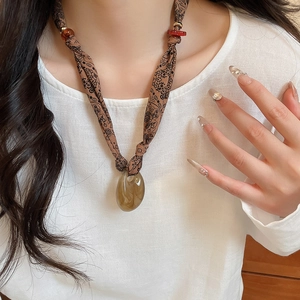 Close-up of brown paisley fabric cord necklace with amber resin heart pendant and red beads