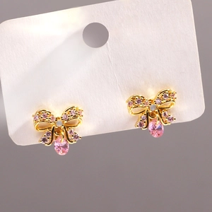 Close-up of golden bow earrings with pink zircons and drop-shaped crystal detail