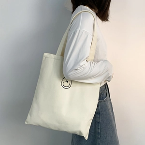 Close-up of minimalist off-white canvas tote bag featuring a black smiley face print