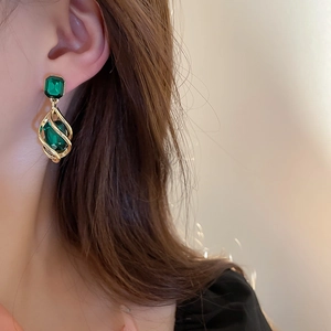 Detailed view of vintage gold earrings with emerald green rectangular gemstones on model