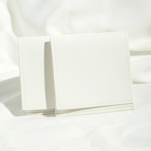 Detail of white PU leather pouches with drawstring flap on soft white textured fabric