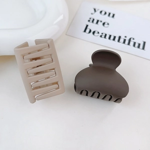 Detail of matte hair clips in beige and dark brown on a white minimalist tray
