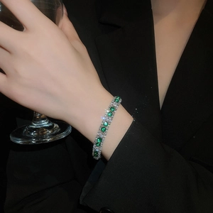 Close-up of a silver tennis bracelet with emerald green stones on a model's wrist