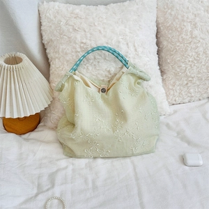 Detailed view of light green tote bag featuring floral embroidery and woven handles