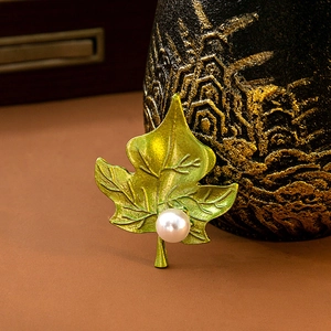Detail of green leaf brooch with realistic veins and centered white pearl on a dark blazer