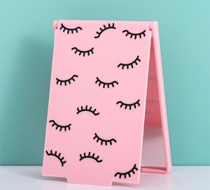Detail of pink foldable makeup mirror featuring eyelash pattern on a standing rectangle frame