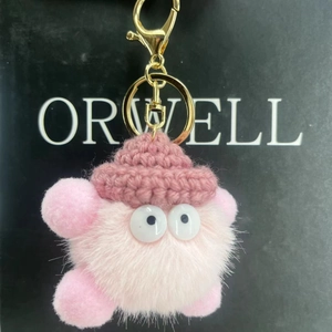 Detailed close-up of a pink fuzzy keychain with a knit hat and cute googly eyes