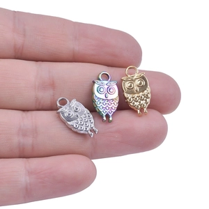 Three owl pendants in gold, silver, and rainbow colors held on fingers for size reference