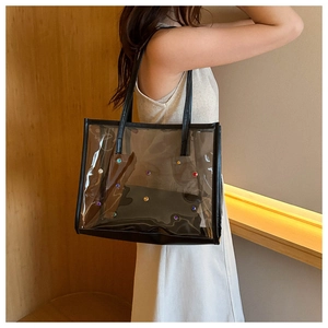 Transparent PVC tote bag with colorful studs and black straps worn by a model