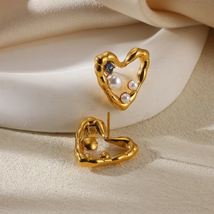 Detail of heart-shaped gold studs with white pearls and a blue gemstone on white stone