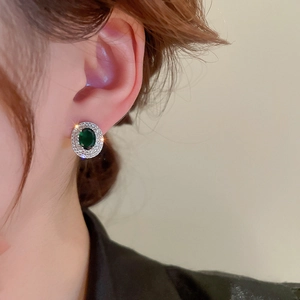 Macro detail of emerald oval stud earring with double halo zirconia setting on ear