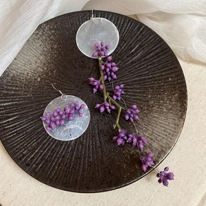 Detailed close-up of purple berry tassels and pearl white shell drop earrings set on a tray