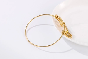 Detail of adjustable gold bangle with hollow round pendant on white ceramic plate