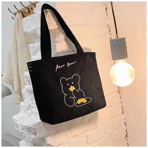 Close-up of black corduroy tote bag with bear embroidery hanging on a brick wall