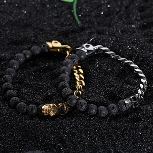 Lava stone bead bracelet with metal skull details in silver and gold on dark sand