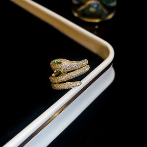 Macro detail of gold plated snake ring featuring sparkling pavé crystals and green gemstone eyes