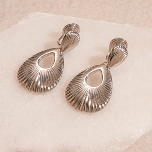 Close-up of silver teardrop hollow earrings with radiant texture on stone background