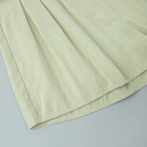 Close-up of light green cotton linen fabric showing pleated texture and double-stitched hem