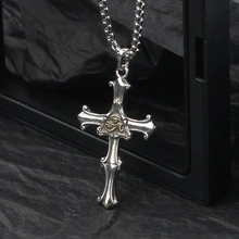 Detailed view of vintage silver and gold cross pendant with Eye of Horus motif on black background