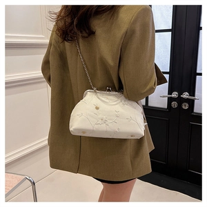 Detail of white floral embroidery and vintage metal clasp on elegant crossbody chain bag