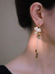Détail de boucles d'oreilles à pompon avec feuilles de ginkgo dorées et perles oeil de tigre