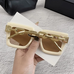 Detalle de gafas de sol cuadradas con montura crema y patillas de cadena dorada