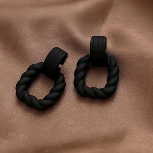 Macro view of matte black twisted square stud earrings on brown silk fabric background