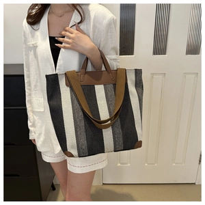 Detailed view of striped canvas tote bag with brown leather handles worn by model