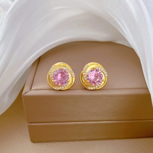 Macro shot of gold spiral earrings with pink gemstone and small white diamonds in a box