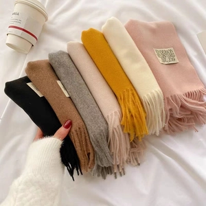 Multiple colors of double-sided faux cashmere scarves with fringe edges stacked on an arm