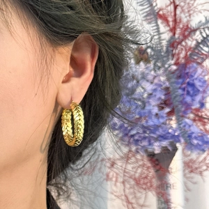 Gold braided texture hoop earring worn by a model with soft floral background