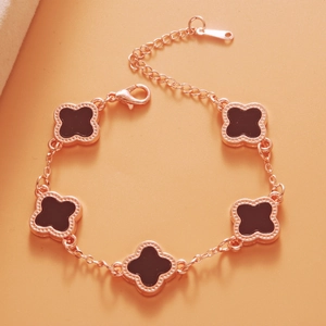 Close-up of rose gold clover bracelet with black motifs on a warm orange background
