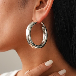 Close-up of a large polished silver hoop earring worn by a model for a chic look