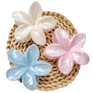 Floral frangipani hair claw clips in white pink and blue on a woven mat background