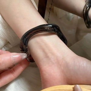 Detail of irregular wave resin bangle with dark tortoise shell texture on female wrist
