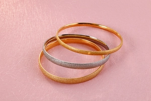 Close-up of stacked gold and silver titanium bangles with a sparkling frosted finish
