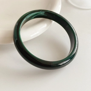 Macro shot of dark green marbled resin bangle with polished round texture on a white tray