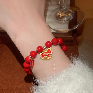 Detail of red glass bead bracelet with gold pony charm and lucky Chinese inscription