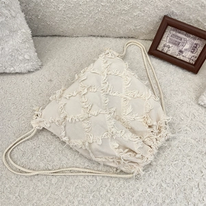 Detail of cream tassel canvas backpack with textured diamond pattern and rope straps