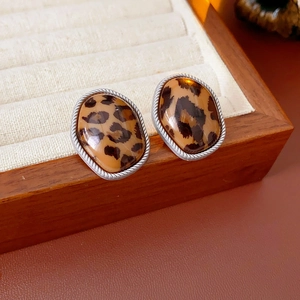 Détail macro de boucles d'oreilles ovales léopard avec bordure en corde argentée sur tissu