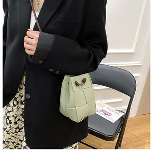 Close-up of light green woven bucket bag with brown drawstring on model in black blazer