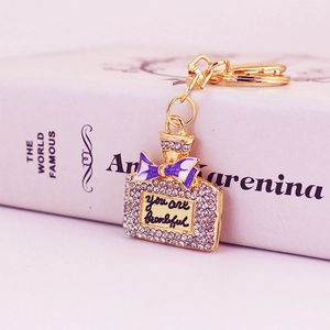 Eleganter Parfümflaschen-Schlüsselanhänger mit Strass und lila Schleife auf einem Buch