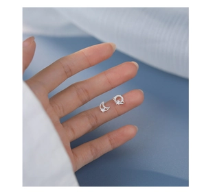 Miniature S925 silver planet moon studs held in fingers to show delicate small size