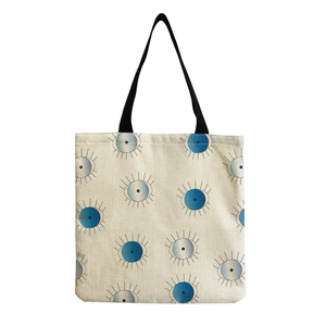Detail of canvas tote bag with evil eye print and black ribbon handles on white base