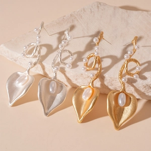 Elegant gold and silver metallic leaf earrings with pearls on decorative stone