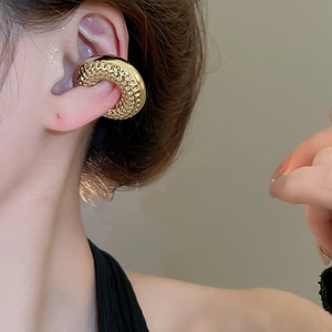 Gros plan d'un large ear cuff doré présentant un motif texturé en nid d'abeille sur la surface